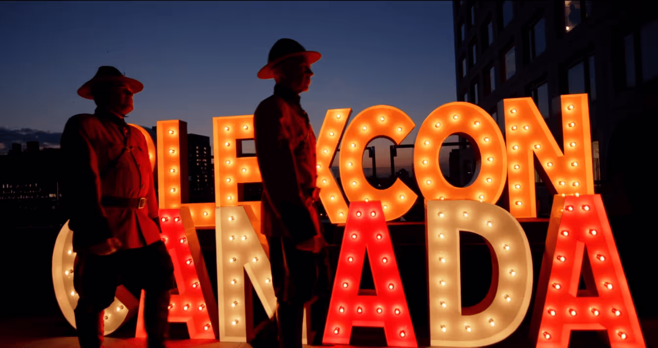 Silhouetted figures standing beside illuminated "Welcome Canada" sign at night